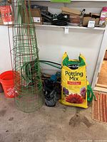 Overall lot showing tomato cages, bucket, potting mix, hose, tote