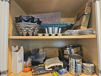 Cabinet shelf with bundt pan, silicone molds, cooling rack, mini tart pans, boxed foil pie pans, loaf pan and other bakeware