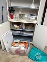 Cabinet showing disposable tableware, plastic cups, cutlery, aluminum pans, mason jars, storage tote