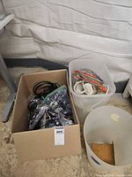 Cardboard box and plastic bin containing assorted cables and accessories