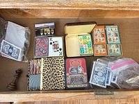 Drawer view showing assorted card decks in tins, loose Bicycle cards, domino tiles and chess bishop