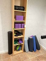 Shelf and floor showing yoga blocks, rollers, resistance bands, medicine ball, bolster and mats