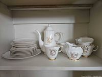 Teapot, creamer, second jug, stack of saucers and serving plate on shelf