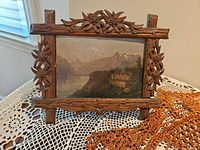 Front view of carved wood frame with landscape print displayed on lace table cover