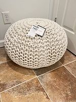 Full view of cream cotton knit rope ottoman pouf with tags attached