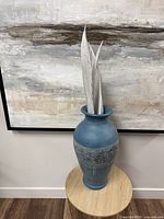 Full view of blue ceramic vase with faux leaves against wall art
