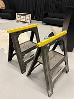 Front angled view of both folding sawhorses showing yellow top rails and molded shelves