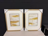 Two matching framed abstract gold and white art pieces with corner protectors