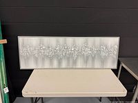 Full view of rectangular silver textured wall art on table