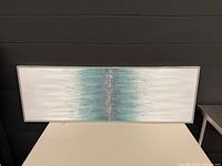 Full view of framed abstract teal and white artwork on table