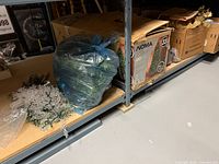 Overall shelf view showing Noma tree box, bagged greenery, silver garland, additional decoration box