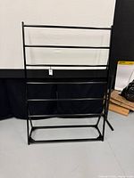 Full frontal view of black metal rug rack showing six horizontal bars and overall structure