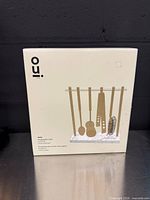 Front of sealed box showing illustration of four hanging bar tools on marble stand, brand name Oui visible