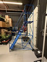 Side view of blue mobile platform ladder showing extended top platform, handrails, steps, and casters