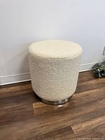 white faux fur cylindrical ottoman with chrome base on wood floor