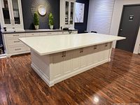 Overall view of island showing stone countertop, paneled base, hardware, surrounding cabinetry for scale