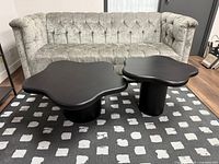 Both black coffee tables in front of sofa showing size difference and design