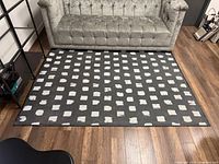 Full view of rug placed on wooden floor showing pattern and size relative to sofa