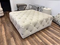 Full view of square beige tufted ottoman on wood floor