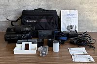 Complete lot overview showing camcorder, batteries, charger, tapes, film items, paperwork and Tamrac bag