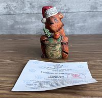 Front view of hand-carved bear figurine with Santa hat and sack, certificate visible
