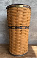 Front view of tall cylindrical Longaberger basket showing weave, accent band and brass plate