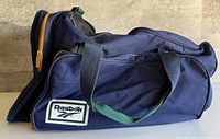 Front of navy Reebok duffle showing logo patch, handles, yellow zipper