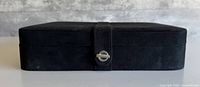Closed black suede jewelry box showing exterior and strap closure