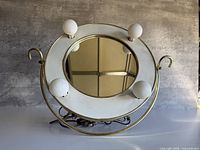 Front view showing round mirror, four bulbs, gold frame, white surround