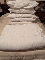 Stack of four white pillows and folded white duvet on bed