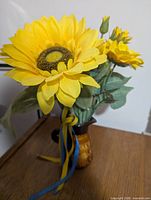 Brown ceramic jug vase holding yellow artificial sunflowers with blue-yellow ribbons