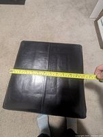 Top view of black faux leather ottoman with tape measure showing width