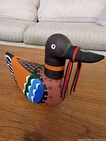Full left side view of painted wooden duck with cord on beak