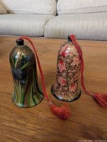 Pair of lacquer bell ornaments with red tassels shown upright on table