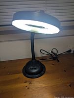 Black gooseneck desk lamp with circular head on wooden surface