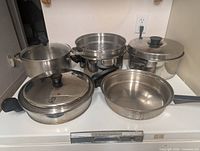 Five stainless steel cookware pieces with lids on stovetop