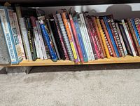 Row of mixed cookbooks on low shelf, Company’s Coming titles visible