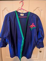 Front view of royal blue Thai silk jacket with green trim and chest floral appliqué