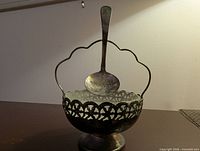 Front view of silver-plated pedestal bowl with ladle suspended from handle