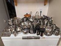 Large assortment of stainless steel bowls, pots, mugs, creamers, egg cups, toast rack on appliance top
