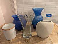 Group of six larger vases including blue glass, clear hexagonal, white ceramic, enamel vessel