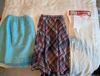 All three items laid out: turquoise skirt, plaid skirt, white knit kit
