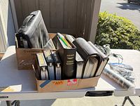 Binders and manuals in cardboard box alongside binoculars and additional binder