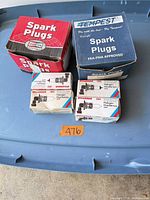 Closed view of four product boxes: Tempest spark plugs, red spark plug box, two Sylvania halogen bulbs