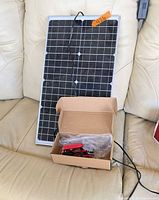 Solar panel leaning on sofa with charger box and cables visible