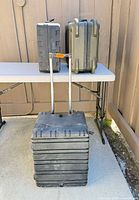 Rolling trolley case and two hard-shell cases on table