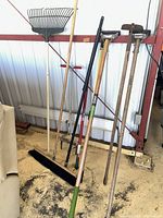 Group of long-handled tools including rake, broom, post hole digger, hoes