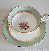 Teacup nested on saucer showing floral interior, mint green border, gold trim