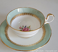 Teacup front on saucer showing mint green rim, gold gilt, floral interior