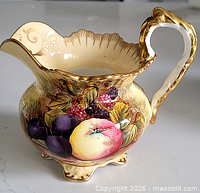 Left side view of cream jug showing fruit motif, gold trim, four feet